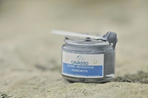 Un pot en verre posé sur le sable sur lequel est posé une spatule présentant un échantillon d'une pâte gris anthracite