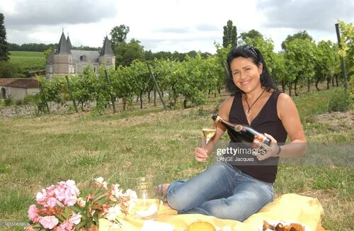 Béatrice Cointreau pose un verre de Champagne Gosset à la main devant les vignes et le Château Fontpinot chez Cognac Frapin